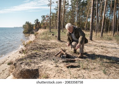 Mature Man Making Campfire With Pleasure Smile While Kneeling At The Seashore