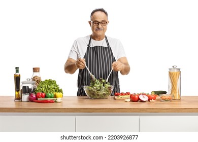 Mature Man Mixing A Salad In A Bowl On A Kitchen Counter With Vegetables Isolated On White Background