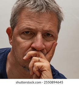 Mature man in a moment of deep contemplation, hand resting on chin, with a thoughtful, introspective expression against a neutral background - Powered by Shutterstock