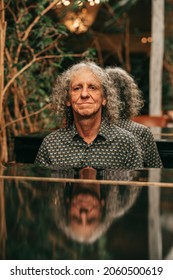 Mature man musician with curly gray hair is reflected on surface of grand piano, playing music, happy. Active senior, photo. Lifestyle portrait, people with passion