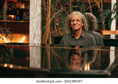 Mature man musician with curly gray hair, reflected on surface of grand piano, playing music, happy. Active senior, photo. Lifestyle portrait, people with passion.