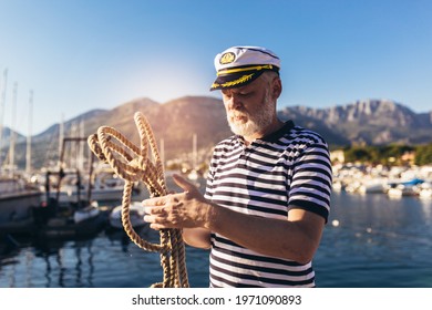 Mature man near the sea dressed in a sailor's shirt and hat holding a sailor rope