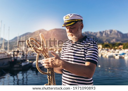 Mature man near the sea dressed in a sailor's shirt and hat holding a sailor rope