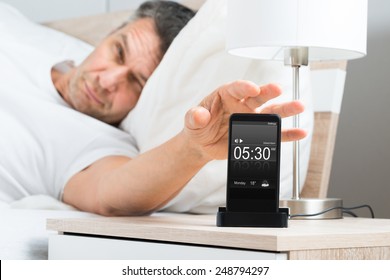 Mature Man On Bed With Cell Phone On Nightstand - Powered by Shutterstock