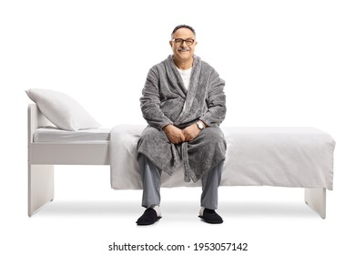 Mature Man In Pajamas And A Robe Sitting On A Bed Isolated On White Background