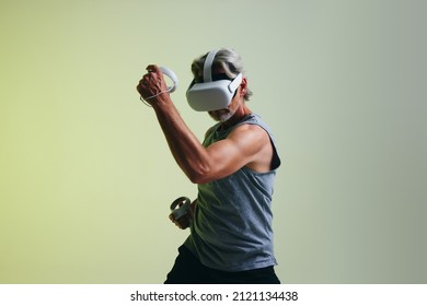 Mature man playing games while wearing a virtual reality headset. Man enjoying a 3D simulation while standing against a studio background. - Powered by Shutterstock