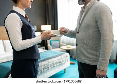 Mature Man Pointing At Display Of Tablet Held By Hotel Manager In Bedroom