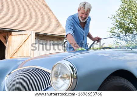 Mature Man Polishing Restored Classic Sports Car Outdoors At Home      