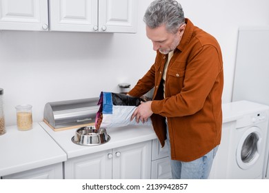 Mature Man Pouring Dog Food In Bowl In Kitchen