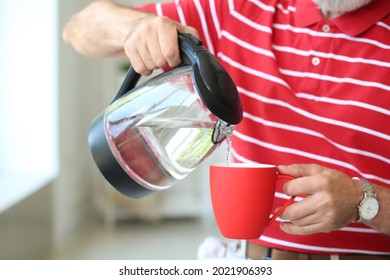 Mature Man Pouring Hot Water From Electric Kettle Into Cup At Home