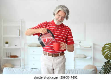 Mature Man Pouring Hot Water From Electric Kettle Into Cup At Home