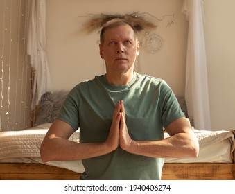 Mature Man Practicing Yoga And Meditating At Cozy Home With Hands Holding Together