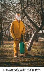 Mature man in protection suit spraying tree with chemicals in the orchard before winter.
