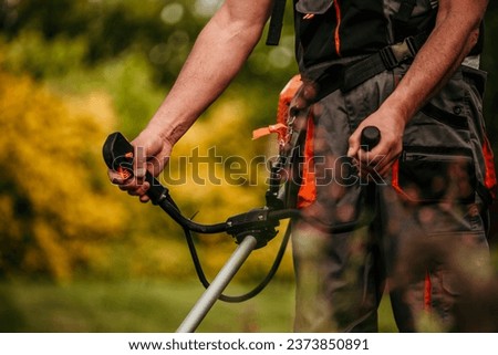 A mature man in a protective work suit showcasing his gardening prowess while operating a grass trimmer in his scenic outdoor space