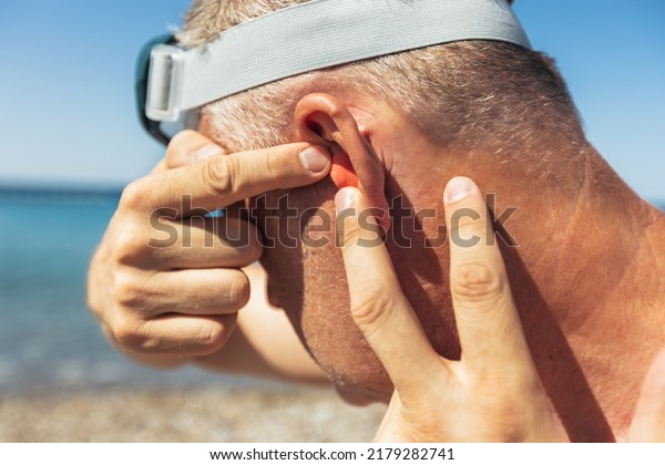 Mature man putting silicone ear plugs, surfers\
earplugs, swim plugs