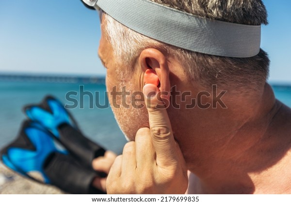 Mature man putting silicone ear plugs, surfers\
earplugs, swim plugs