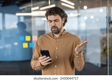 Mature man with a puzzled expression checking his smartphone. Office setting with blurred background. - Powered by Shutterstock