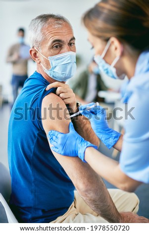 Mature man receiving coronavirus vaccine at his shoulder at vaccination center.