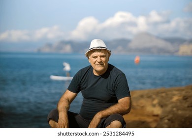 A mature man relaxes on the seashore on the rocks and looks at the blue sea.
 - Powered by Shutterstock