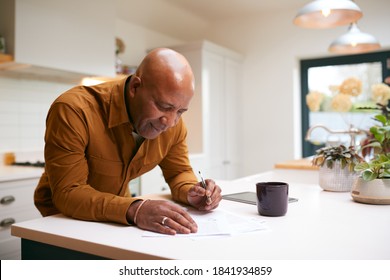 Mature Man Reviewing And Signing Domestic Finances And Investment Paperwork In Kitchen At Home - Powered by Shutterstock