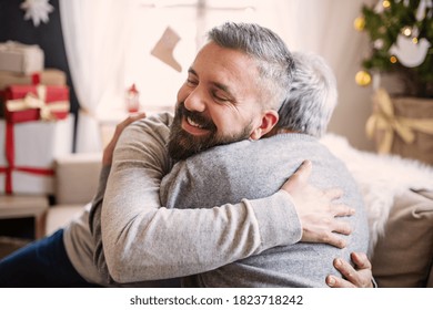 Mature man and senior father indoors at home at Christmas, hugging. - Powered by Shutterstock