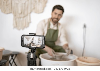 Mature man shaping clay vase using potter's wheel and recording video blog with smartphone. Craftsmanship and creativity showcased. - Powered by Shutterstock