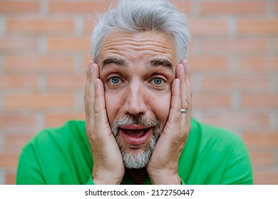 Mature Man With Shocked, Amazed Expression Touching His Face On Street Background.