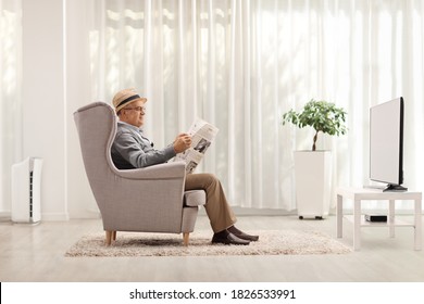 Mature man sitting in an armchair and reading a newspaper in a living room at home - Powered by Shutterstock