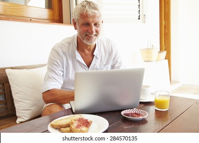 Mature Man Sitting At Breakfast Table Using Laptop