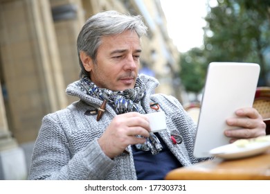 Mature Man Sitting At Coffee Shop Table With Tablet