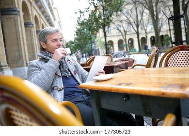 Mature Man Sitting At Coffee Shop Table With Tablet