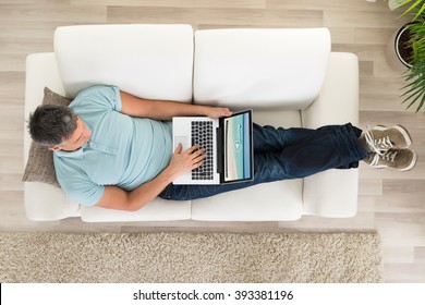Mature Man Sitting On Sofa With Laptop At Home