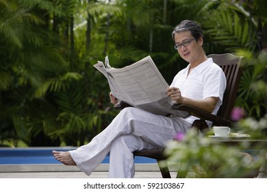 Mature man sitting outdoors, reading newspaper