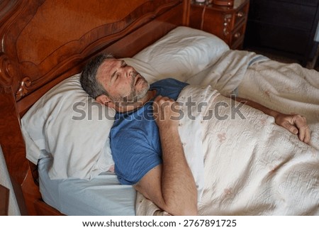 Mature man sleeping in a comfortable bed. His mouth is open, suggesting snoring or sleep apnea, depicting a restless night
