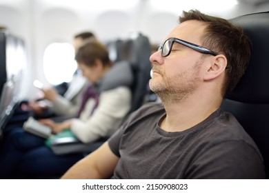 Mature man sleeping while traveling by an airplane. Tired passenger napping during flying in aircraft. Long-haul flights. - Shutterstock ID 2150908023