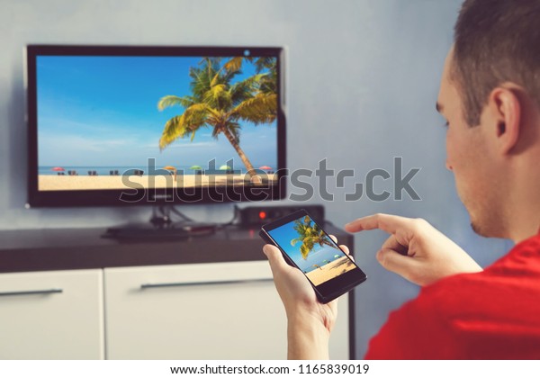 Mature Man With Smartphone Connected\
To A TV Watching Movie At Home. relaxed man with smartphone\
connected to a tv and envisioning photos in\
networking