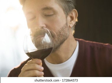 Mature Man Smelling Glass Of Red Wine At Home