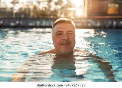 Mature man smiling in a sunlit pool, sunlight at hotel reflecting off the water around him. Spa, retreat, relaxation and Beauty and body care concept image  - Powered by Shutterstock