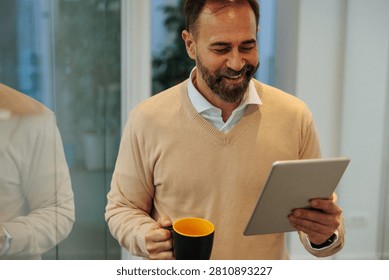 Mature man smiling while casually using a tablet and drinking coffee, reflecting business communication and digital lifestyle