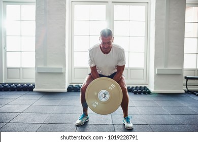 Mature Man In Sportswear Standing Alone In A Gym Focused On Lifting Weights During A Workout