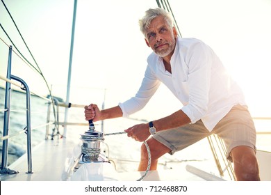 Mature man standing on the deck of his boat using a winch while out for a sail on a sunny afternoon - Powered by Shutterstock