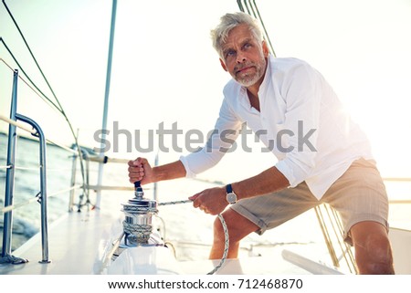 Mature man standing on the deck of his boat using a winch while out for a sail on a sunny afternoon
