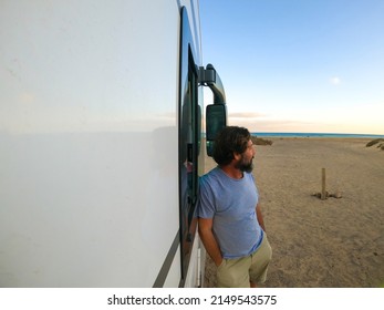 Mature Man Standing Outside A Modern Camper Van Admiring The Ocean And Enjoying The Beach. Travel People Lifestyle Concept. Freedom Camp Site. Adult Looking Horizon And Nature