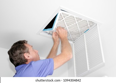 Mature Man Taking Out A Dirty Air Filter From A Home Ceiling Air Return Vent. Male Removing A Dirty Air Filter With Both Hands In A House From A HVAC Ceiling Air Vent.