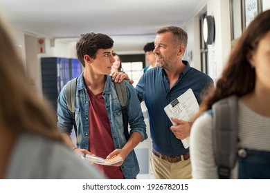 Mature man talking to high school student in hallway at the end of the lesson. Senior professor in conversation with guy student in campus. Teacher talking to encourage young man after exam.