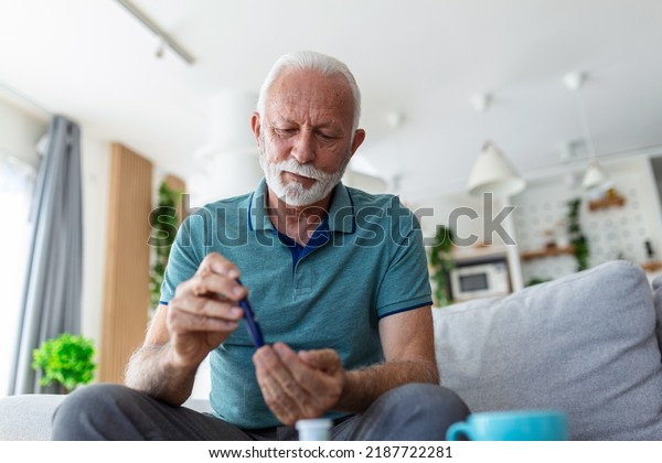 Mature\
man testing for high blood sugar. Man holding device for measuring\
blood sugar, doing blood sugar test. Senioir man checking blood\
sugar level by glucometer and test stripe at\
home
