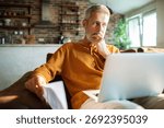 Mature man thinking while using laptop at home