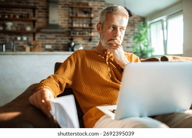 Mature man thinking while using laptop at home