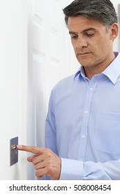 Mature Man Turning Off Light Switch At Home