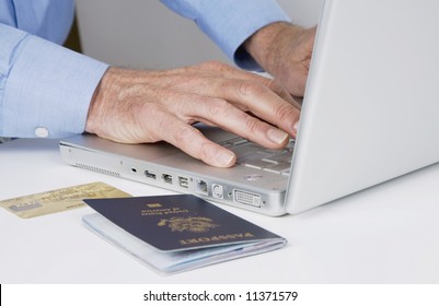 Mature Man Typing On Laptop Computer With Passport And Credit Card Next To Him